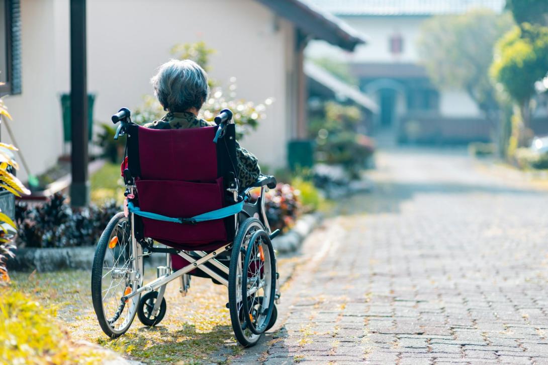 Ältere Person im Rollstuhl auf einem Weg