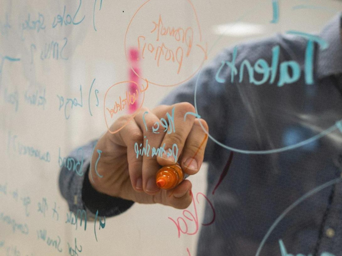 Person skizziert Ideen auf einem Glas-Whiteboard